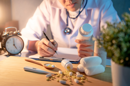 Male Asian doctor looking at pill bottle on his hand writing on clipboard. Doctor working with medicine paperwork on the desk in clinic or hospital. Medical treatment and health care concepts.の写真素材