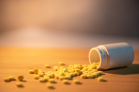 Pills spilling out of pill bottles with digital thermometer and pharmaceutical spoon on wooden table. Prescription medicine and medical treatment background conceptsの写真素材