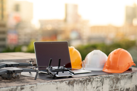 Drone, smartphone, laptop computer and protective helmet at construction site. Using unmanned aerial vehicle (UAV) for land and building site survey in civil engineering project.の写真素材