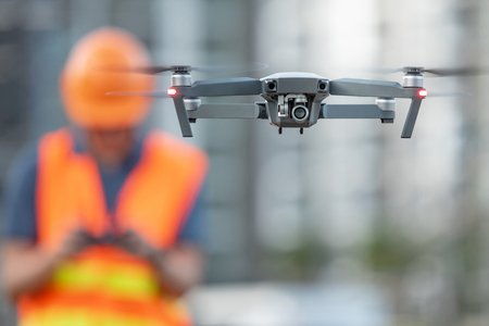 Young Asian engineer flying drone over construction site. Using unmanned aerial vehicle (UAV) for land and building site survey in civil engineering project.の写真素材