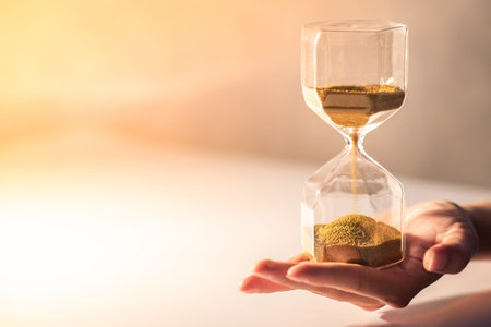 Close up of brown sand running through the shape of modern hourglass on male hand.Time passing and...