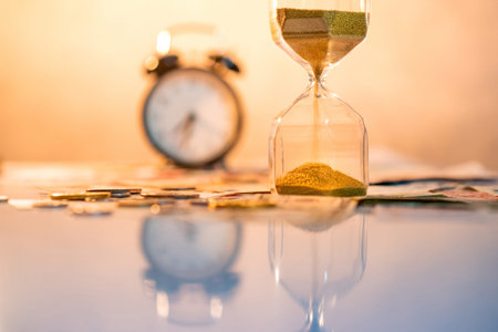 Reflection of sand running through the shape of hourglass on table with currency and clock in the...