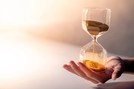 Close up of gold sand running through the shape of modern hourglass on male hand.Time passing and running out of time. Urgency countdown timer for business deadline concept with copy spaceの写真素材