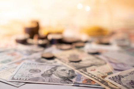 Various of international money coin and banknote with blurred hourglass in the background. Time investment with currency exchange concept. Focus on dollar banknote.の写真素材