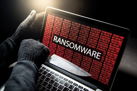 Male hacker threading laptop computer with knife showing on screen with red digital binary ransomware warning. Cyber attack and internet data security conceptの写真素材