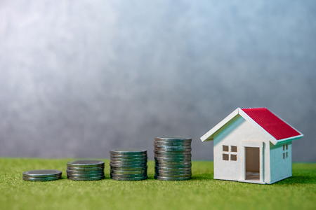 Real estate investment or Home mortgage loan rate. Property ladder concept. Coins stack, house model and table clock on green grass. Investment and business growth backgroundの写真素材