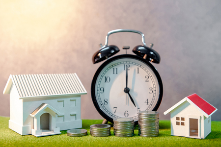 Real estate investment or Home mortgage loan rate. Property ladder concept. Coins stack, house model and table clock on green grass. Investment and business growth backgroundの写真素材