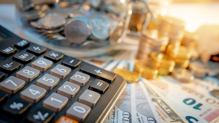 Calculator with currency glass jar and gold coins stack, dollar and euro banknotes on the table. Compound interest rate calculation or financial investment business conceptsの写真素材