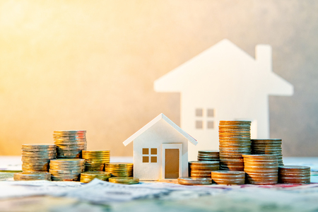 Real estate or property investment. Home mortgage loan rate. Saving money for retirement concept. Coin stack on international banknotes with house model on table. Business growth backgroundの写真素材