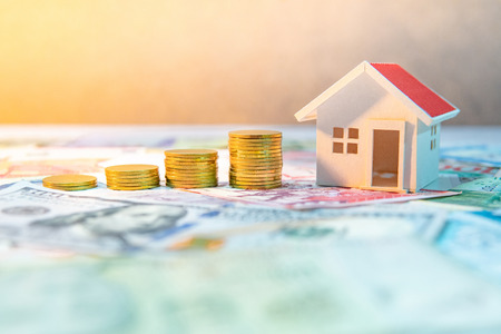 Real estate or property investment. Home mortgage loan rate. Saving money for retirement concept. Coin stack on various of international banknotes with house model on table. Business growth concept.の写真素材