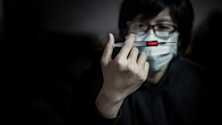 Young man in the mask using syringe for red drug injection. Drug abuse and addiction conceptの写真素材