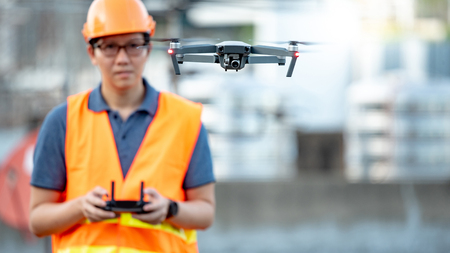 Young Asian engineer man flying drone over construction site. Using unmanned aerial vehicle (UAV) for land and building site survey in civil engineering project.の写真素材