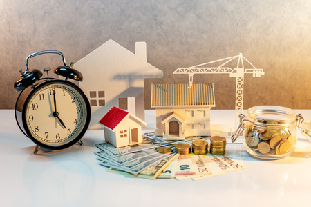 Real estate or property development. Construction business investment concept. Home mortgage loan rate. Coin stack on international banknotes with clock, house and crane models on the table.の写真素材