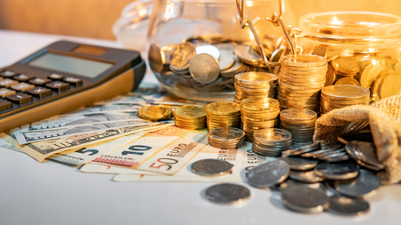 Calculator with coins stack and spilling out of money bag, dollar and euro banknotes on the table. Compound interest rate calculation or financial investment business conceptsの写真素材