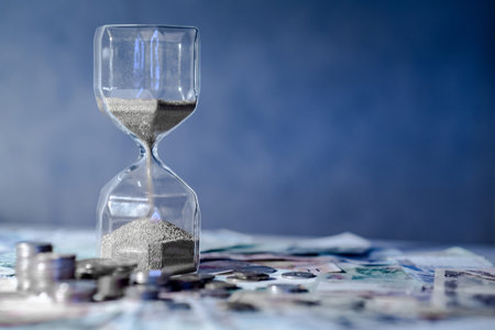 Sand running through the shape of hourglass on table with banknotes and coins of international...