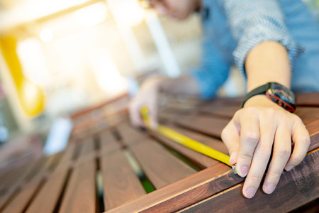 Young Asian man using tape measure for measuring wooden outdoor table in showroom. Shopping furniture for home improvement. Interior design conceptの写真素材