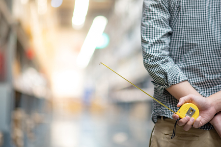 close up of male worker hand holding yellow tape measure in warehouse. Furniture product design measuring conceptの写真素材