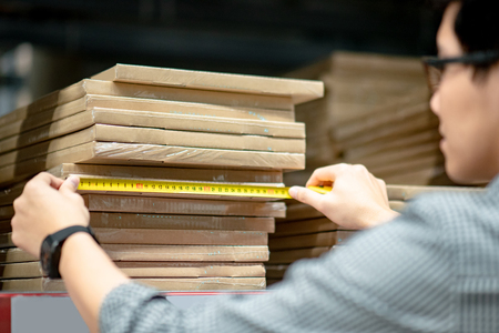 Young Asian man worker using tape measure for measuring dimension of product in cardboard box. Shopping lifestyle in warehouse conceptの写真素材