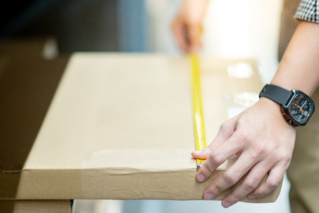 Male worker hand using tape measure for measuring dimension of product in cardboard box. Shopping lifestyle in warehouse conceptの写真素材