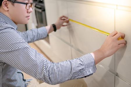Young Asian man using tape measure for measuring modern kitchen counter in showroom. Shopping furniture for home improvement conceptの写真素材