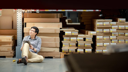 Young Asian man worker doing stocktaking of product in cardboard box on shelves in warehouse by using digital tablet and pen. Physical inventory count conceptの写真素材