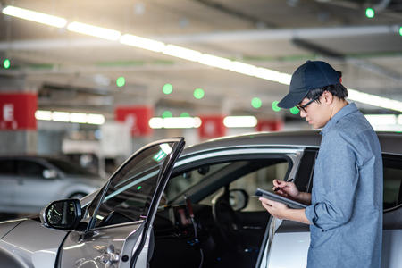 Young Asian auto mechanic holding digital tablet checking car door in auto service garage. Mechanical maintenance engineer working in automotive industry. Automobile servicing and repair conceptの写真素材