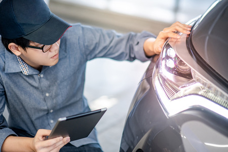 Young Asian auto mechanic holding digital tablet checking headlight in auto service garage.の写真素材