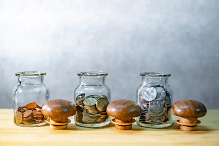 Coins in currency glass jars on wooden table. Saving money for future retirement. Financial business...