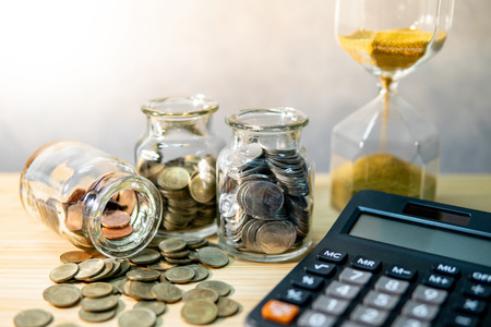 Calculator with coin in currency glass jar and hourglass on wooden table. Compound interest rate calculation. Financial business plan. Time investment conceptの写真素材