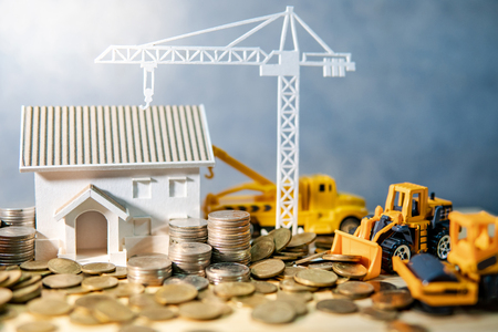 House, crane and construction truck models with gold coins spilling on wooden table. Real estate development or property investment. Home mortgage loan rate. Construction industry business conceptの写真素材
