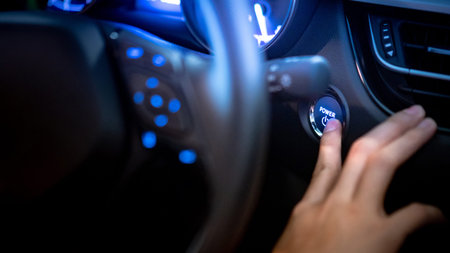 Male driver pushing car engine start-stop button or power ignition button by steering wheel in...