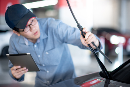 Young Asian auto mechanic holding digital tablet checking windshield wiper in auto service garage. Mechanical maintenance engineer working in automotive industry. Automobile servicing and repairの写真素材