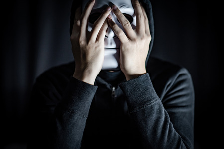Mystery hoody man wearing white mask in the dark room. Anonymous social masking. Major depressive disorder or bipolar disorder. Halloween conceptの写真素材