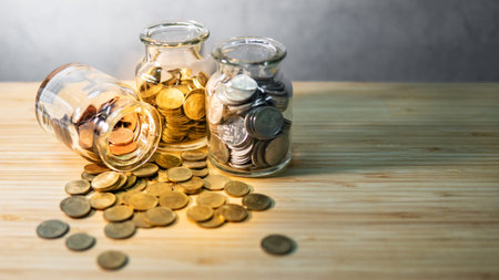 Coins in currency glass jars and spilling on wooden table. Saving money for future retirement....