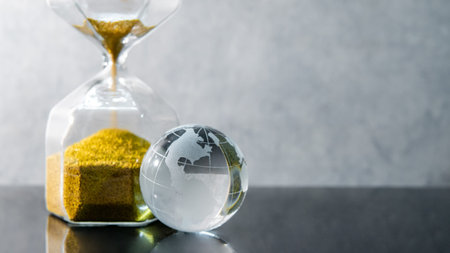 Reflection of gold sand running through the shape of hourglass with world globe crystal glass on...