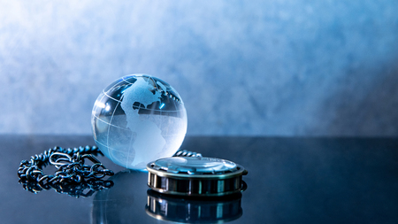 Global business concept. World globe crystal glass and silver pocket watch on glossy table. Time management and investment.の写真素材
