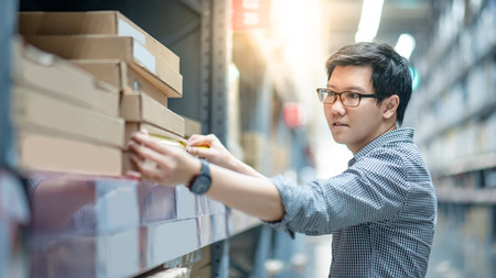 Young Asian man worker using tape measure for measuring dimension of product in cardboard box. Shopping lifestyle in warehouse conceptの写真素材