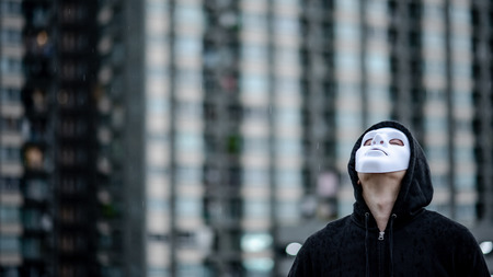 Mystery hoodie man in white mask standing in the rain looking up at the sky on rooftop of abandoned building. Bipolar disorder or Major depressive disorder. Depression conceptの写真素材