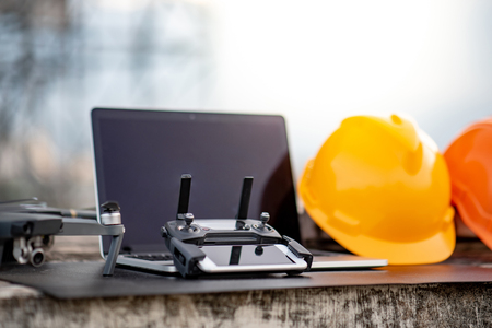 Drone, remote control, laptop computer, smartphone and protective helmet at construction site. Using unmanned aerial vehicle (UAV) for land and building site survey in civil engineering project.の写真素材