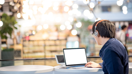 Asian business man listening to music by headphones while working with laptop computer in coworking space. Freelance or digital nomad lifestyle. Online shopping or E-commerce social media on internetの写真素材