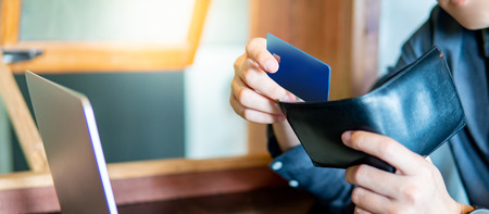 Male hand putting credit card into his wallet. Using credit card for online shopping on laptop computer. Digital payment and cashless society conceptsの写真素材