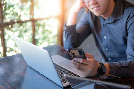 Male hand holding smartphone. Businessman using laptop computer and digital tablet while working in...
