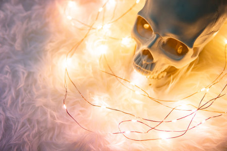 Human skull on white fur carpet with decorative Christmas lights. Studio shot for Halloween festival...