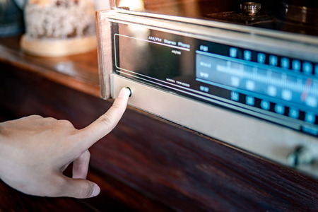 Male hand turning on retro radio by pressing power button. Listen to music or news with old classic radio receiver. Vintage lifestyleの写真素材