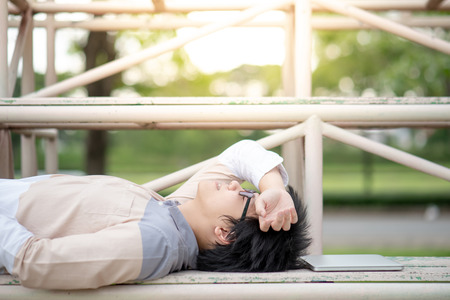 Asian man university student with glasses lying down on cheer stand near his laptop computer. Relaxing lifestyle in the college.の写真素材