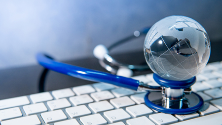 Global healthcare concept. World globe crystal glass on blue stethoscope on white keyboard. Health and medical science. Worldwide wellness business and technologyの写真素材