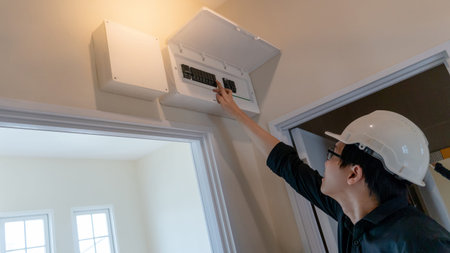 Young Asian electrical technician checking switch on electrical panel board over door frame in the house. Maintenance and installation electric power systemの写真素材
