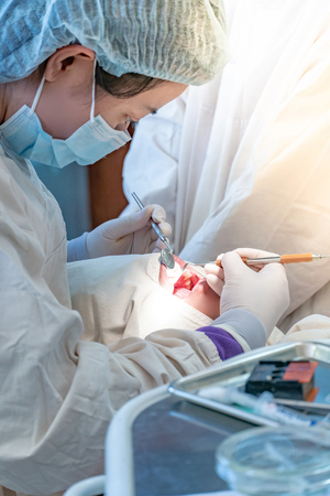 Female Asian dentist using instruments for examining and curing patient teeth in dental clinic. Dental procedure and medical treatment.の写真素材