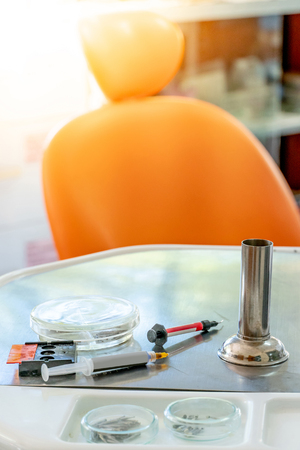 Dental instruments and medical supplies on metal tray in the clinic. Empty orange dental chair and tools for dentist office.の写真素材