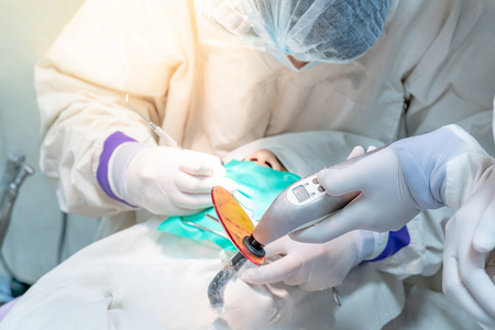 Female dentist and assistant hand using dental curing light and medical instrument supplies for curing patient teeth in the clinic. Dental procedure and treatment concept.の写真素材